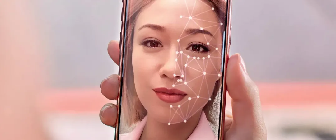 A person holds a smartphone showing a facial recognition interface with digital patterns overlaying their face, conveying a sense of technology and security.